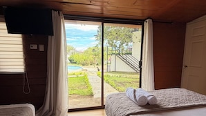 A room with two beds, a TV mounted on the wall, and a sliding glass door leading to an outdoor area with a pool. - Hotel y Centro Turístico Valle Encantado (Gracias)