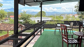A covered outdoor seating area with artificial grass, metal railings, and a view of distant mountains. - Hotel y Centro Turístico Valle Encantado (Gracias)