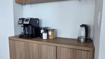 Une petite cuisine équipée d’une machine à café, de bocaux et d’une bouilloire, le tout posé sur un meuble en bois.