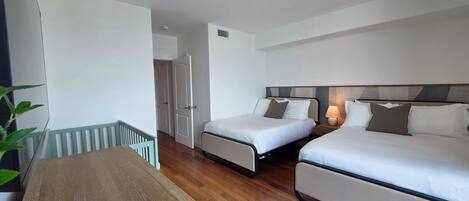 A hotel room with two beds, a wooden table, and a view of the hallway.