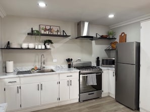 Cozinha moderna com armários brancos, eletrodomésticos de aço inoxidável e bancada de mármore.