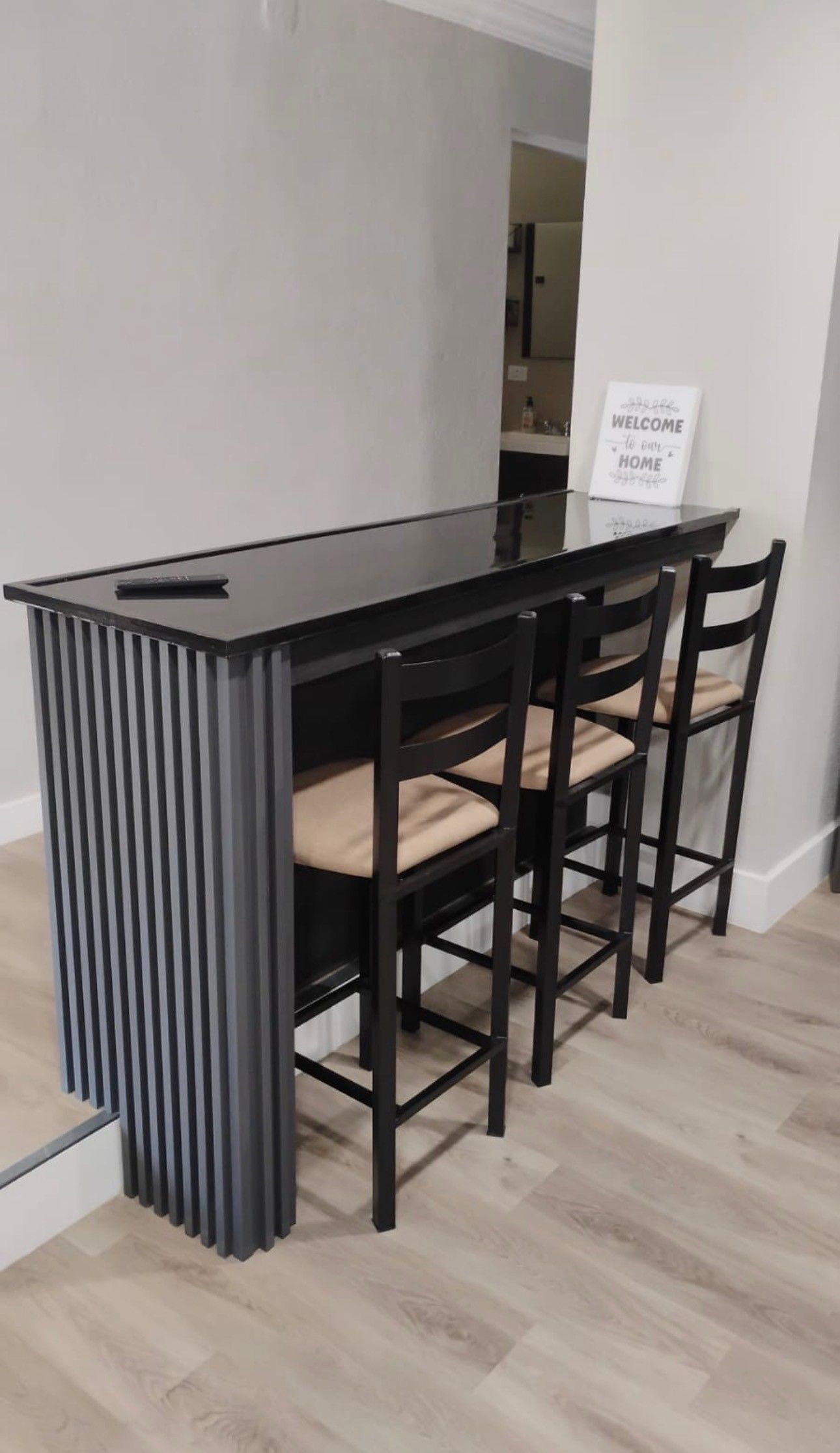 A modern kitchen with a black countertop, four chairs, and a welcome sign.