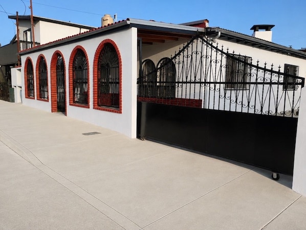Edifício residencial com fachada branca, arcos vermelhos nas janelas e portão de ferro forjado preto.
