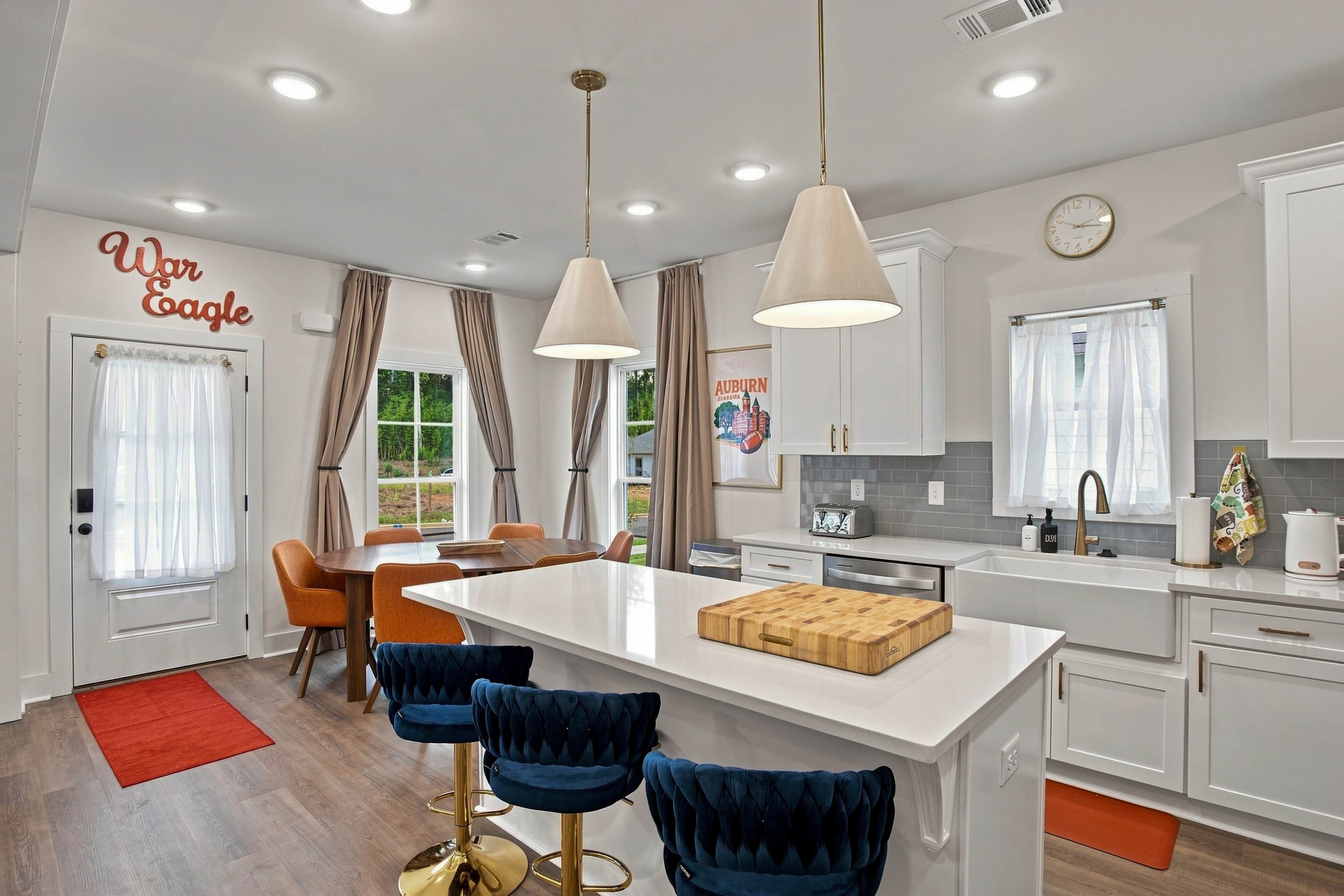 A modern kitchen with a central island, pendant lights, and a dining area with blue chairs.