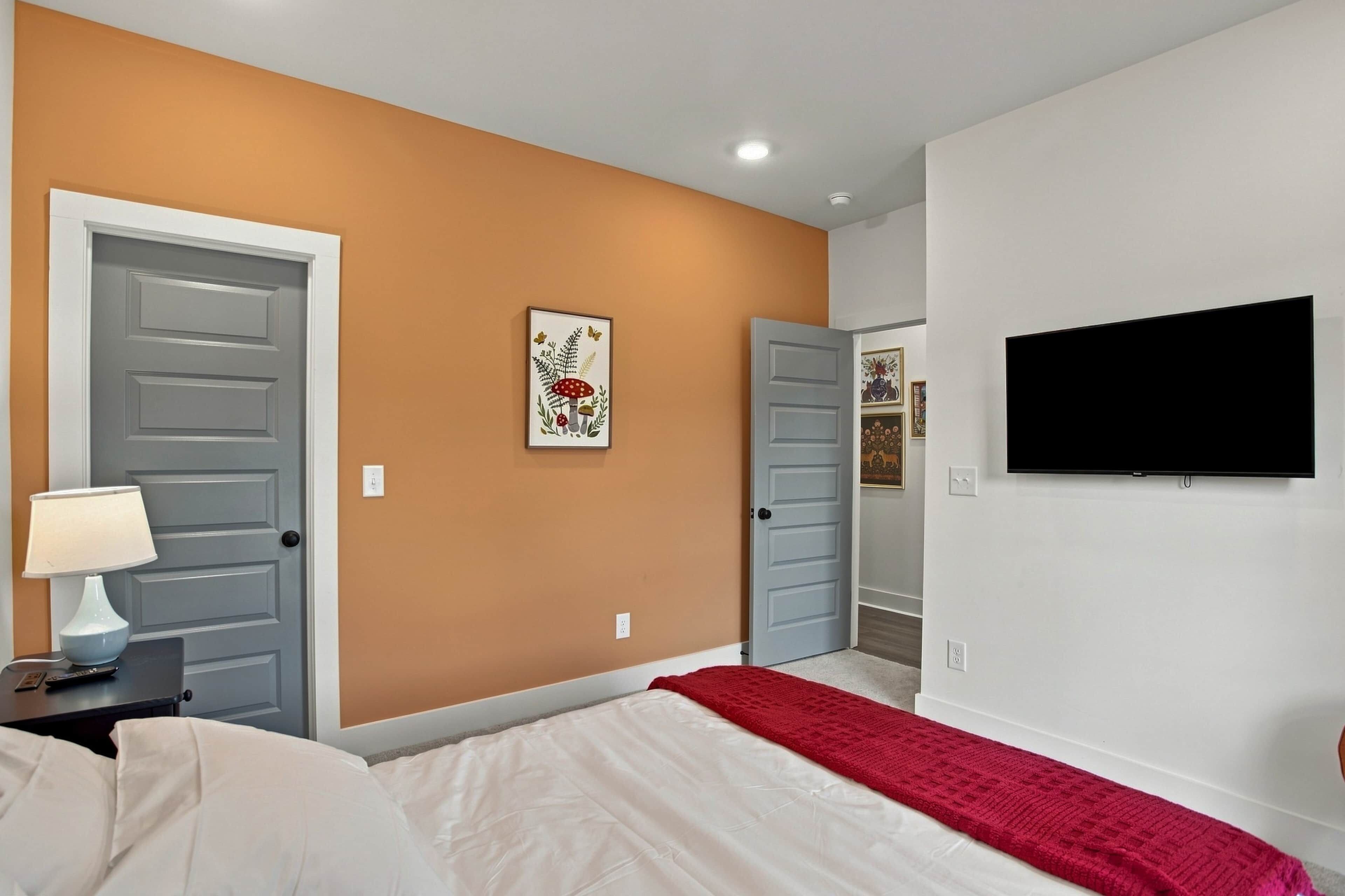 Un dormitorio con cama, televisor, lámpara y un cuadro en la pared.