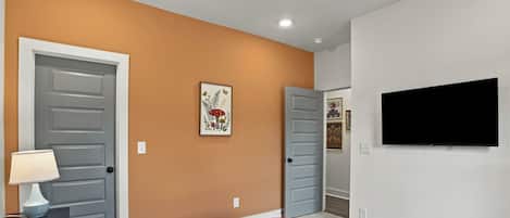 Un dormitorio con cama, televisor, lámpara y un cuadro en la pared.