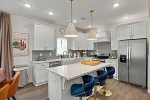 A modern kitchen with white cabinetry, stainless steel appliances, and a central island with bar stools.