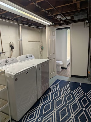 A laundry room with two front-loading washers and dryers, a white door leading to a bathroom, and a patterned rug on the floor.