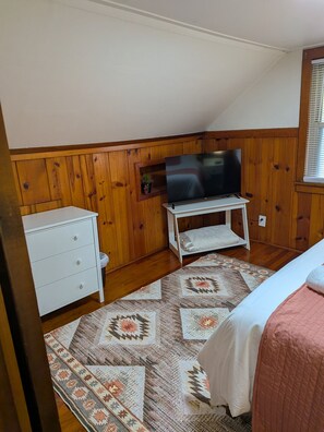 Ein Schlafzimmer mit einem Bett, einer Kommode, einem Fernseher auf einem Tisch und einem gemusterten Teppich.