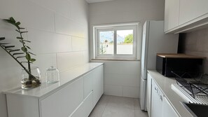 A modern kitchen with white cabinetry, a window with a view, and a plant on the counter. - House with a Sea View in Ericeira • Private Garden • 3 bedrooms (Ericeira)