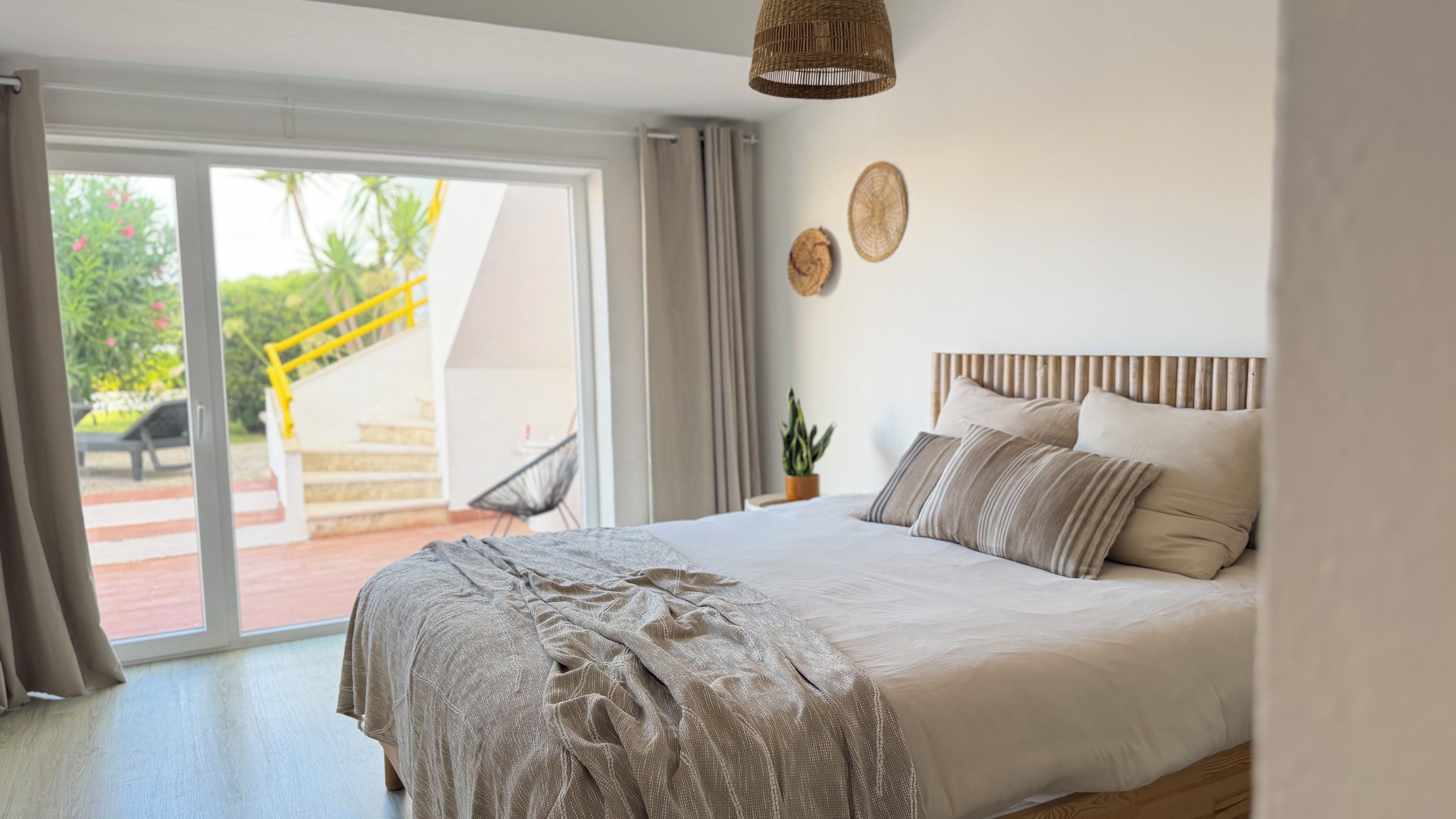 A bedroom with a bed, a potted plant, and a view of a staircase leading outside.