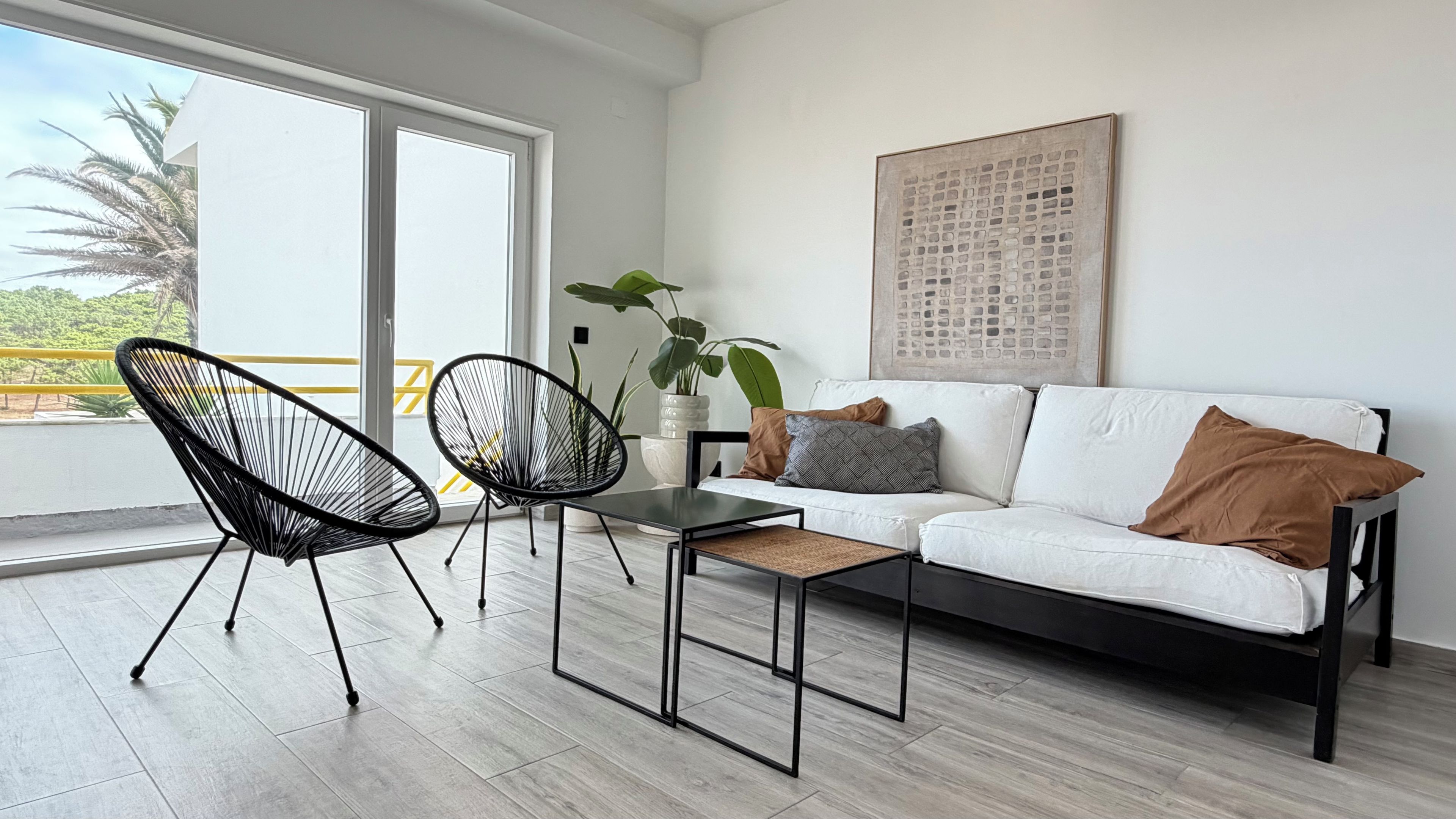 Un salon moderne avec un canapé blanc, deux chaises à armature métallique noire, une petite table noire et une plante en pot.