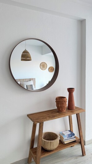 A round mirror on a wall, a wooden console table with a woven basket, a terracotta pot, and a stack of books. - House with a Sea View in Ericeira • Private Garden • 3 bedrooms (Ericeira)