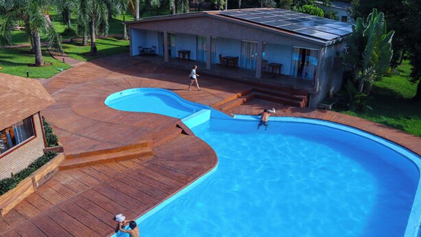 A swimming pool with a wooden deck, a covered patio, and a house with solar panels. - Eco Park Chapada Indaiá (Formosa)