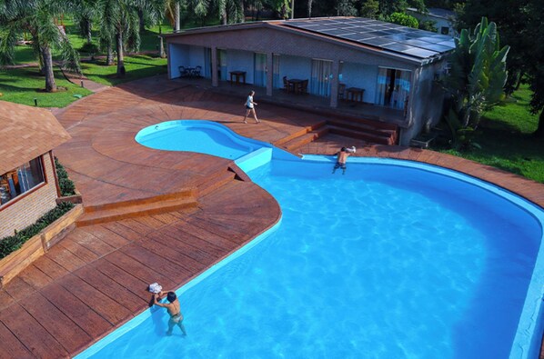 A swimming pool with a wooden deck, a covered patio, and a house with solar panels. - Eco Park Chapada Indaiá (Formosa)