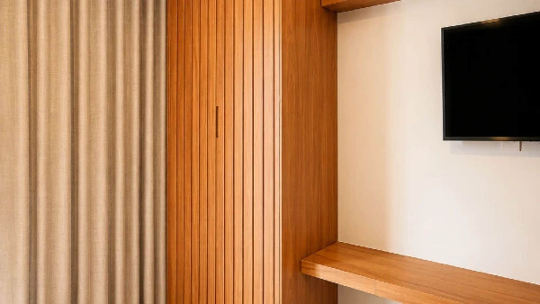 A room with a wooden panel wall, a television mounted on the wall, and a wooden shelf.