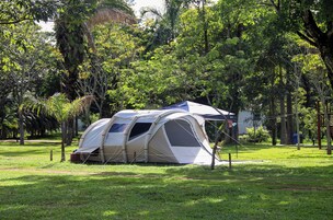 Tenda de camping montada em área gramada, com árvores ao fundo.