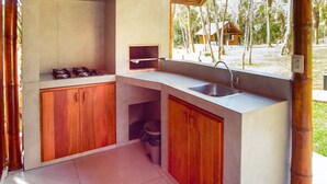 A compact kitchen with wooden cabinets, a sink, and a window overlooking a natural landscape. - Eco Park Chapada Indaiá (Formosa)