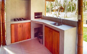 A compact kitchen with wooden cabinets, a sink, and a window overlooking a natural landscape. - Eco Park Chapada Indaiá (Formosa)