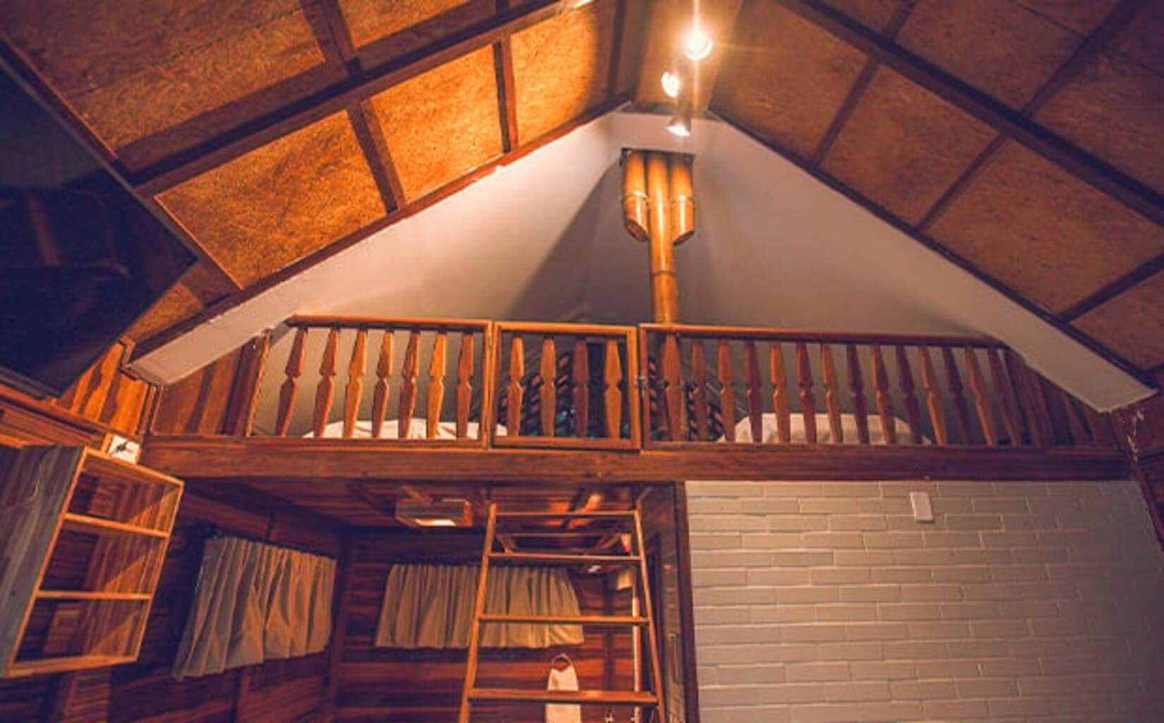 Dormitorio tipo loft con barandal de madera, una escalera y pared de ladrillo blanco.