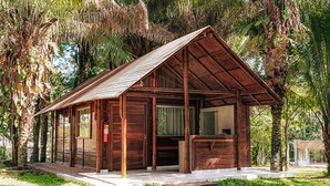 A wooden cabin with a sloped roof, surrounded by lush greenery and palm trees. - Eco Park Chapada Indaiá (Formosa)