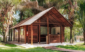 A wooden cabin with a sloped roof, surrounded by lush greenery and palm trees. - Eco Park Chapada Indaiá (Formosa)