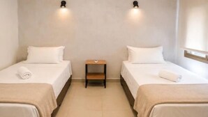 Habitación doble con dos camas, una mesita de noche e iluminación en la pared.