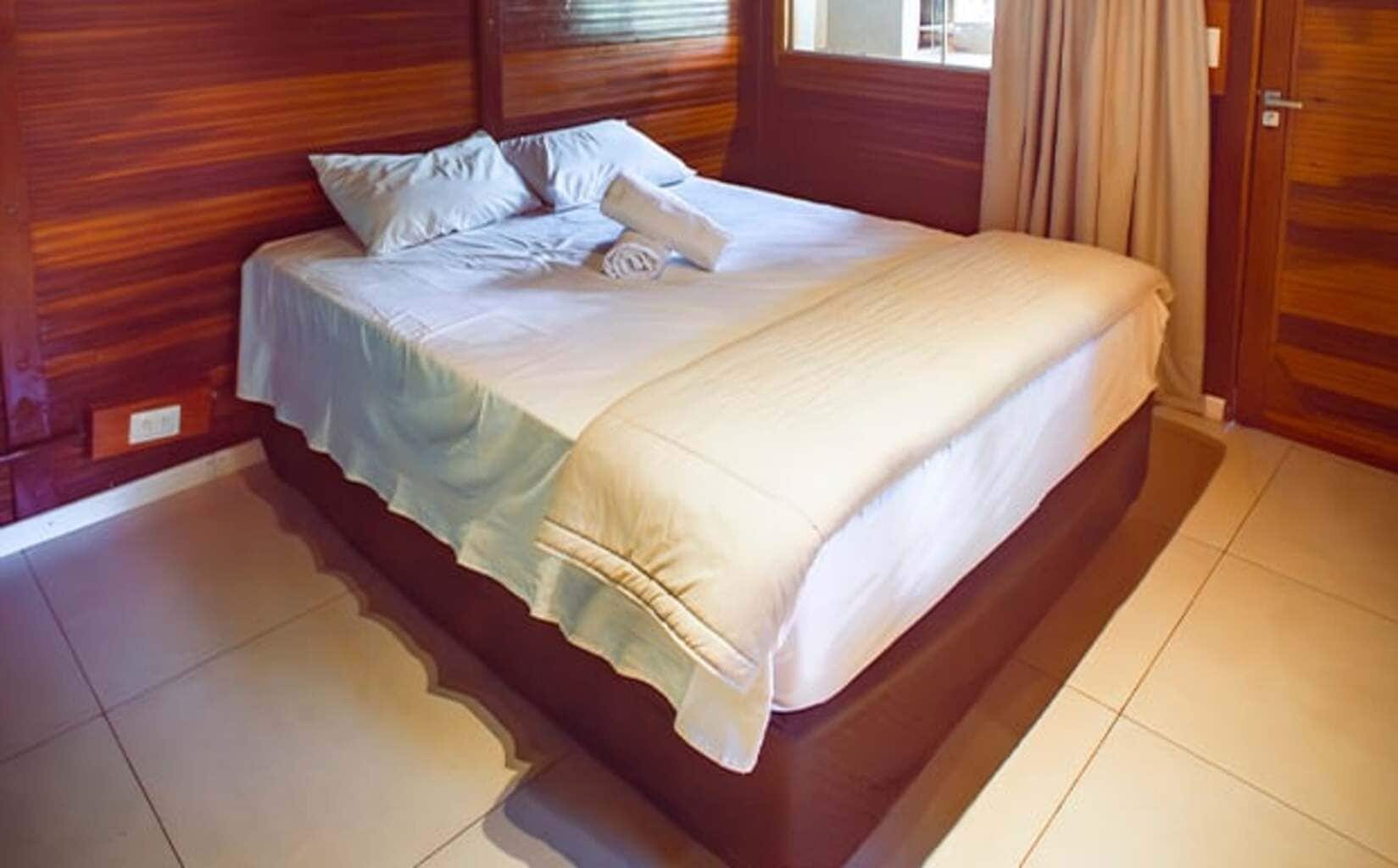 A bed with a wooden headboard and a white bedspread in a room with wooden walls and tiled flooring.