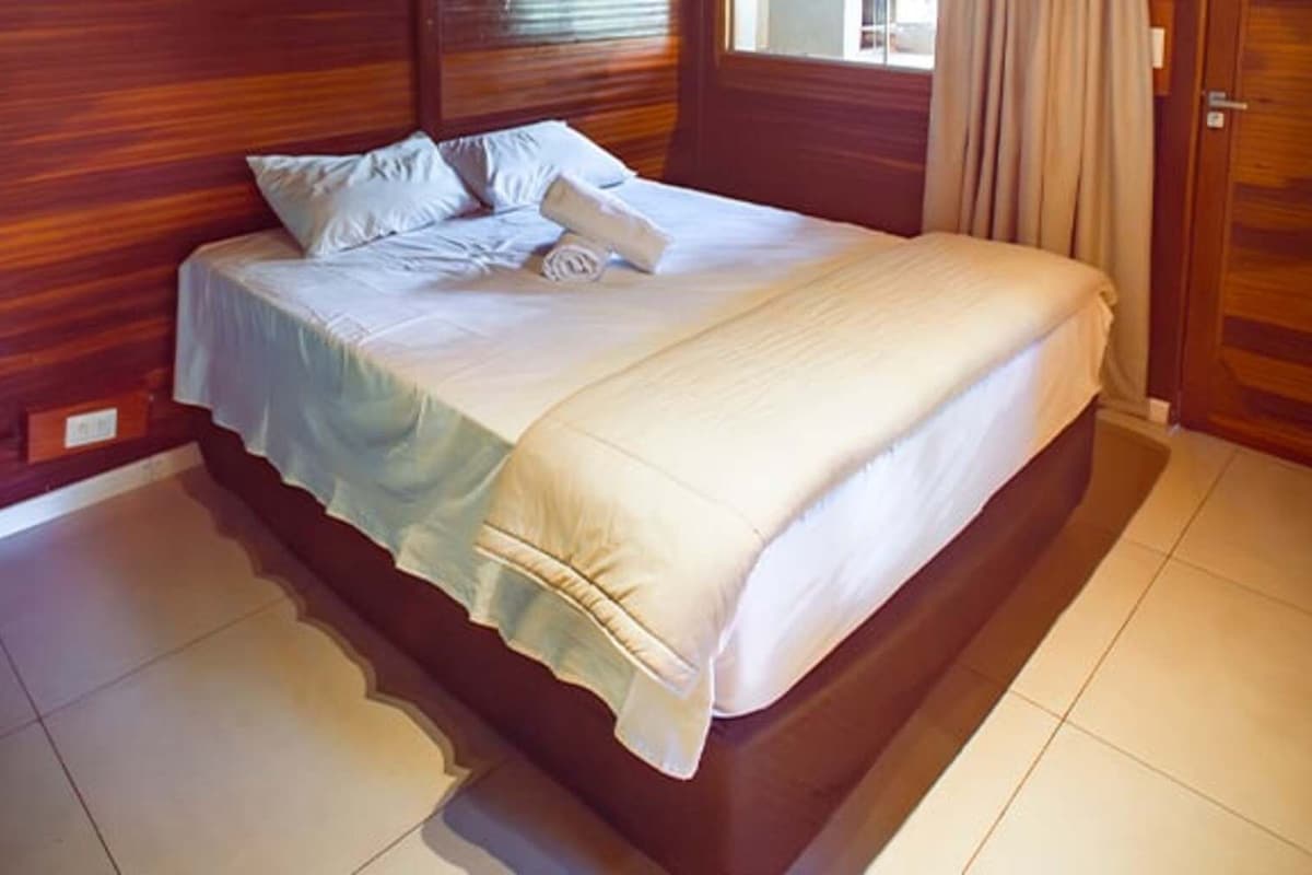 A bed with a wooden headboard and a white bedspread in a room with wooden walls and tiled flooring.