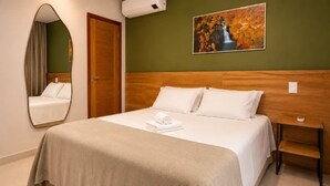 A hotel room with a bed, a wooden headboard, a painting, a mirror, and a bench. - Eco Park Chapada Indaiá (Formosa)