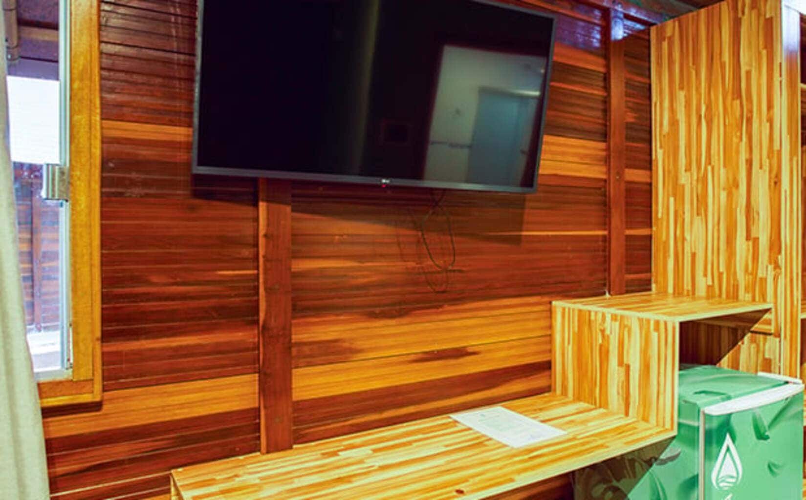 A wooden interior with a flat-screen TV mounted on the wall, a bench, and a trash bin.
