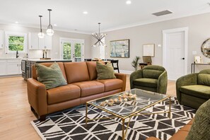 Ein modernes Wohnzimmer mit einem braunen Ledersofa, einem Glastisch und einem Teppich mit geometrischem Muster.
