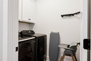 Ein kleiner Hauswirtschaftsraum mit Waschmaschine, Trockner und Bügelbrett.