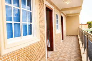Um corredor com piso de azulejos, uma varanda com guarda-corpo de metal e uma parede de tijolos com uma janela.