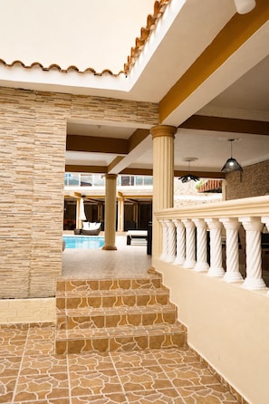 A pool area with steps leading to a balcony, columns, and a ceiling with a wavy design. - Casa Nube | 8 min to SDQ Airport | Private Pool & Jacuzzi (Santo Domingo Este)