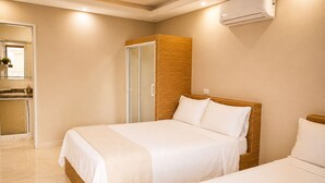 Ein Hotelzimmer mit zwei Betten, einem hölzernen Kopfteil, einem Badezimmer mit Spiegel und einer Klimaanlage.