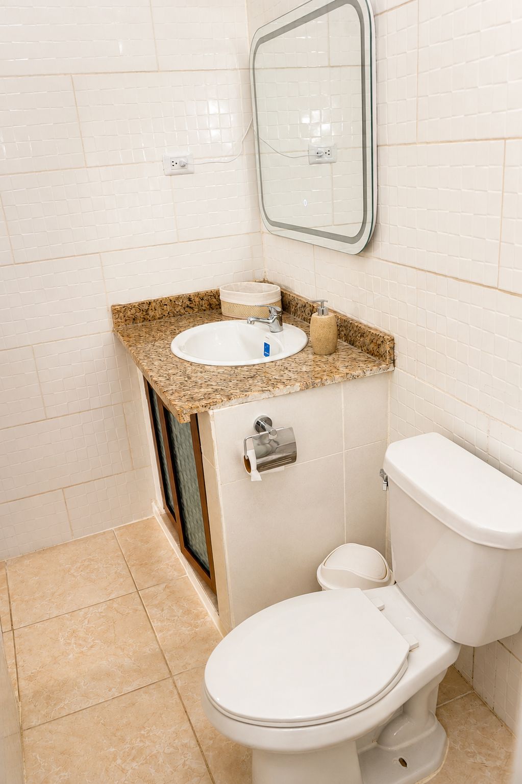 Een badkamer met een wit toilet, een wastafel met een granieten blad en een spiegel boven de wastafel.
