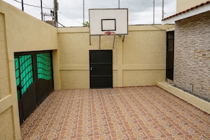 En utomhusbasketplan med en korg, en dörr och en vägg med ett mönstrat ytskikt.