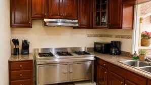 A kitchen with wooden cabinets, a stainless steel stove, a microwave, and a coffee maker. - Casa Nube | 8 min to SDQ Airport | Private Pool & Jacuzzi (Santo Domingo Este)