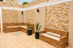 A sunlit outdoor seating area with stone walls and wooden benches. - Casa Nube | 8 min to SDQ Airport | Private Pool & Jacuzzi (Santo Domingo Este)