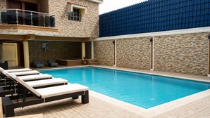 A swimming pool with lounge chairs, a covered seating area, and a stone wall. - Casa Nube | 8 min to SDQ Airport | Private Pool & Jacuzzi (Santo Domingo Este)