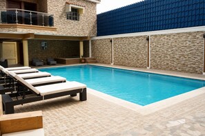 Ein Pool mit Liegestühlen, einer überdachten Sitzgruppe und einer Steinmauer.