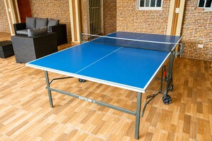 Ett bordtennisbord med hjul, en soffa och en tegelvägg i bakgrunden.