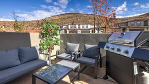 Eine Terrasse im Freien mit Grill, Sitzgelegenheiten und Blick auf eine hügelige Landschaft.