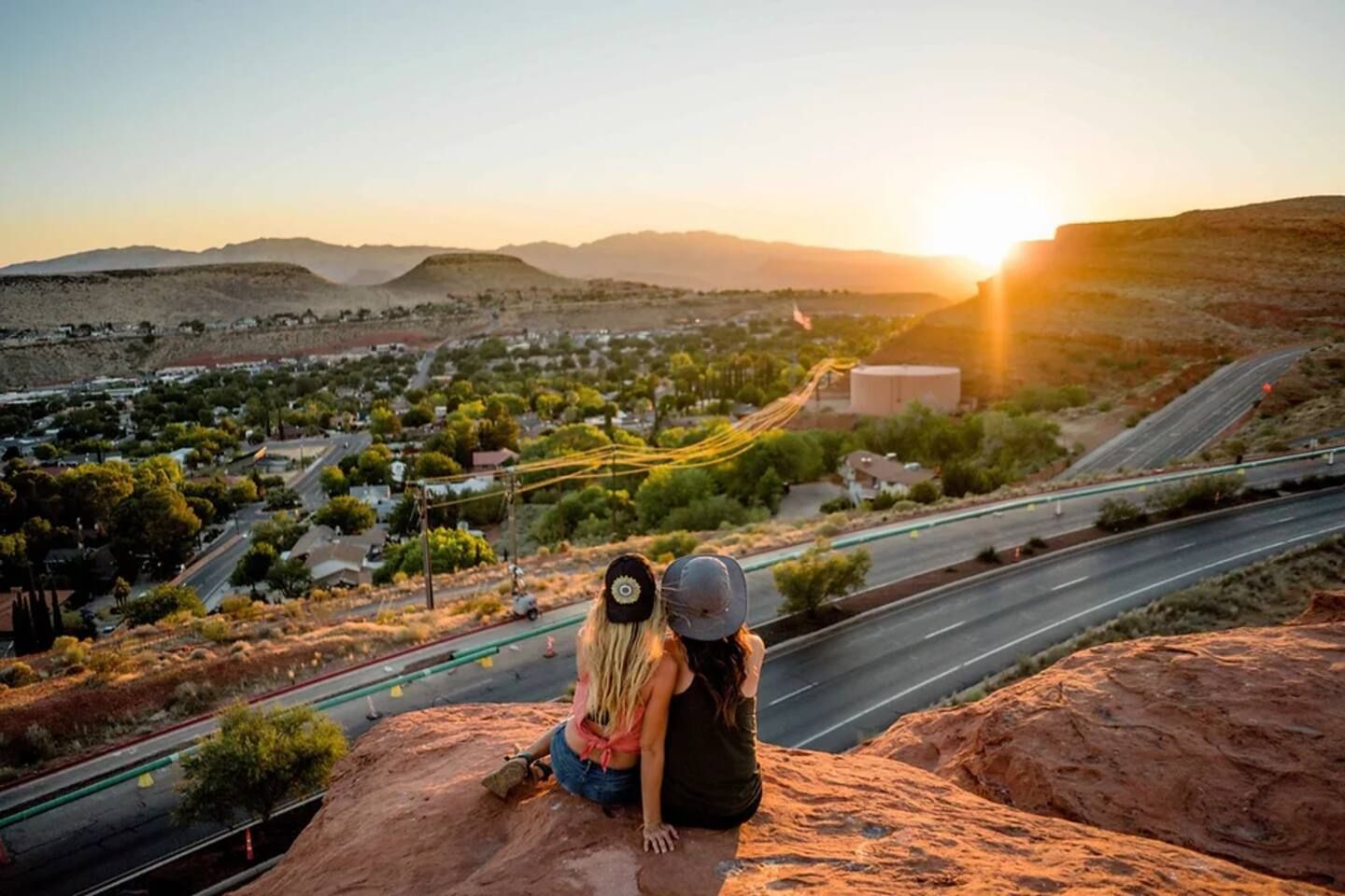 A person sitting on a rock overlooking a town with a road and hills in the background.