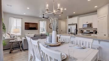 A modern kitchen with white cabinetry, a central island, and a dining area with white chairs and a table.