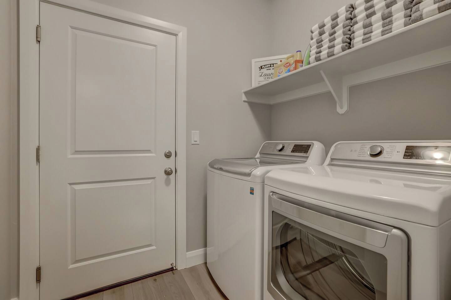 A laundry room with two front-loading washing machines and a shelf above containing laundry supplies.