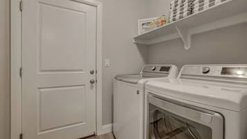 A laundry room with two front-loading washing machines and a shelf above containing laundry supplies.