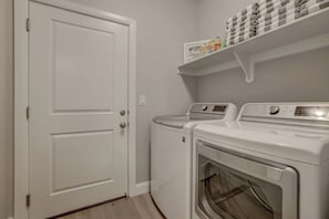 A laundry room with two front-loading washing machines and a shelf above containing laundry supplies. - Hot Tub, Heated Pool with Slide, Pickleball, Bunk Beds,  2PM Check Out (Washington)