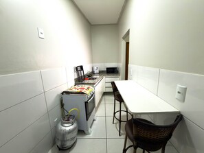A compact kitchen with a gas stove, microwave, and a small dining table with chairs. - CONDOMÍNIO SONHARE - 103 (ANAPOLIS)